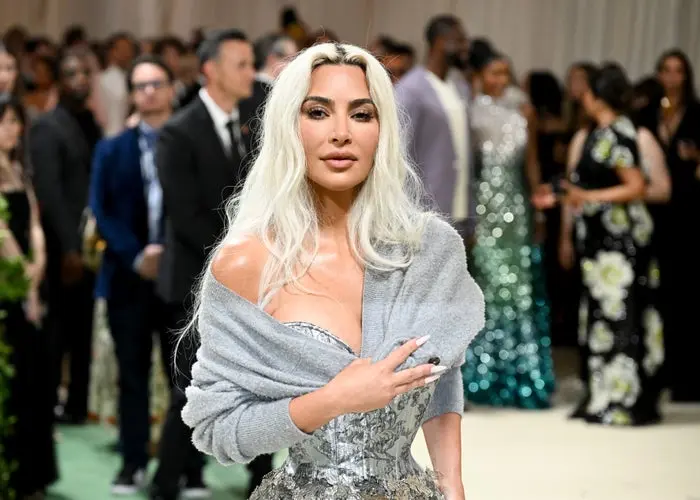 کیم کارداشیان در لباس شیک، بدون شانه، براق، با موهای بلند و موج‌دار بر روی فرش قرمز شلوغ