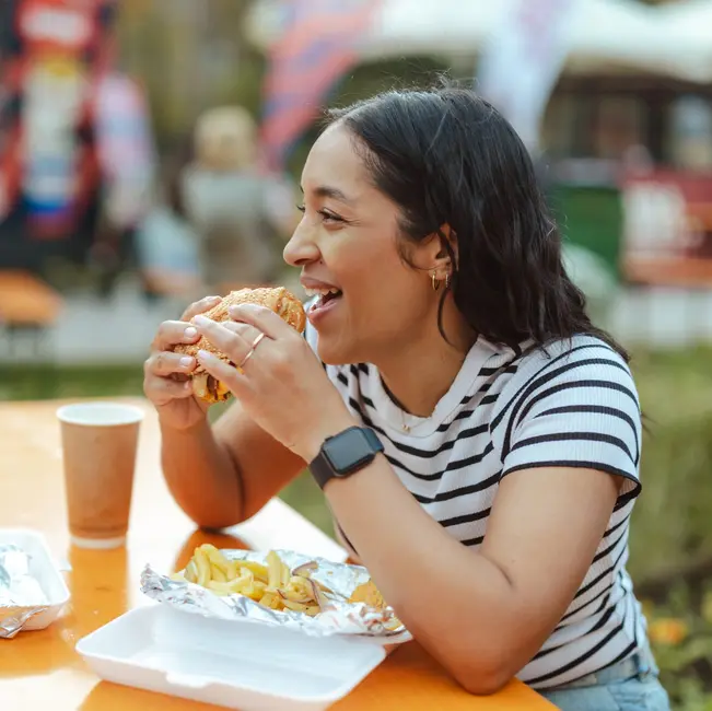 زن در یک رویداد خوراکی بیرونی، همراه دوستش از برگر لذت میبرد