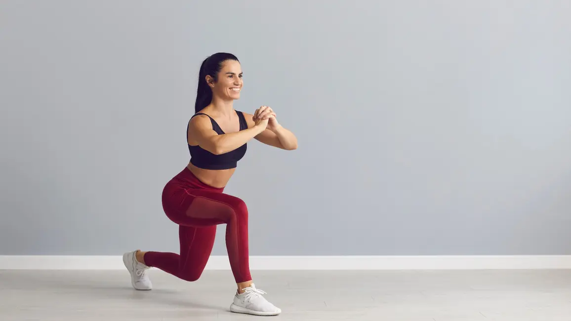 زنی در حال انجام حرکت لانژ کرتسی (curtsy lunge) در یک استودیو با پسزمینه خاکستری