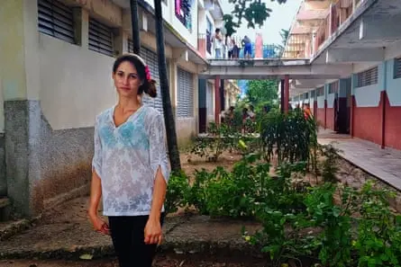 زنی با دست بند مو و پیراهن سفید بین خانهها ایستاده است