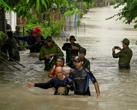 غیرنظامیها و سربازان در آب تا کمر قدم میزنند، در کنار خانهها بر روی خیابانی سیلزده