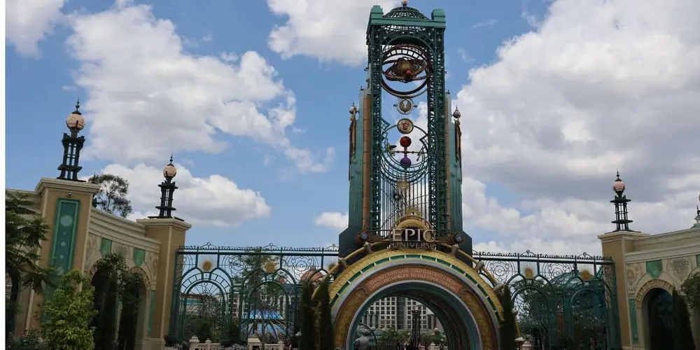 بهدرگاهی بلند، تزئینی و پرجلوه با قوس بزرگی که «Epic Universe» نوشته شده است، برجهای تزیینی و ساختارهای شبیه ساعت، که بازدیدکنندگان را به این پارک تفریحی شگفتانگیز تحت آسمان آبی نیمهابری در یونیورسال خوشآمد میگوید