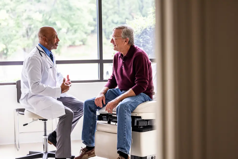 دکتر در روپوش سفید با مرد مسنی که بر روی تخت معاینه نشسته، گفتوگوی گرم و صمیمانهای دارد